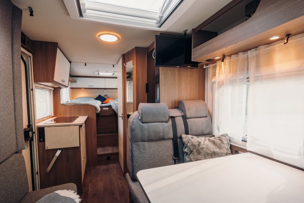 Innenraum Carado Wohnmobil mit Sitzgruppe, Tisch, Dachfenster und Blick zur Küche und zum Heckbett
