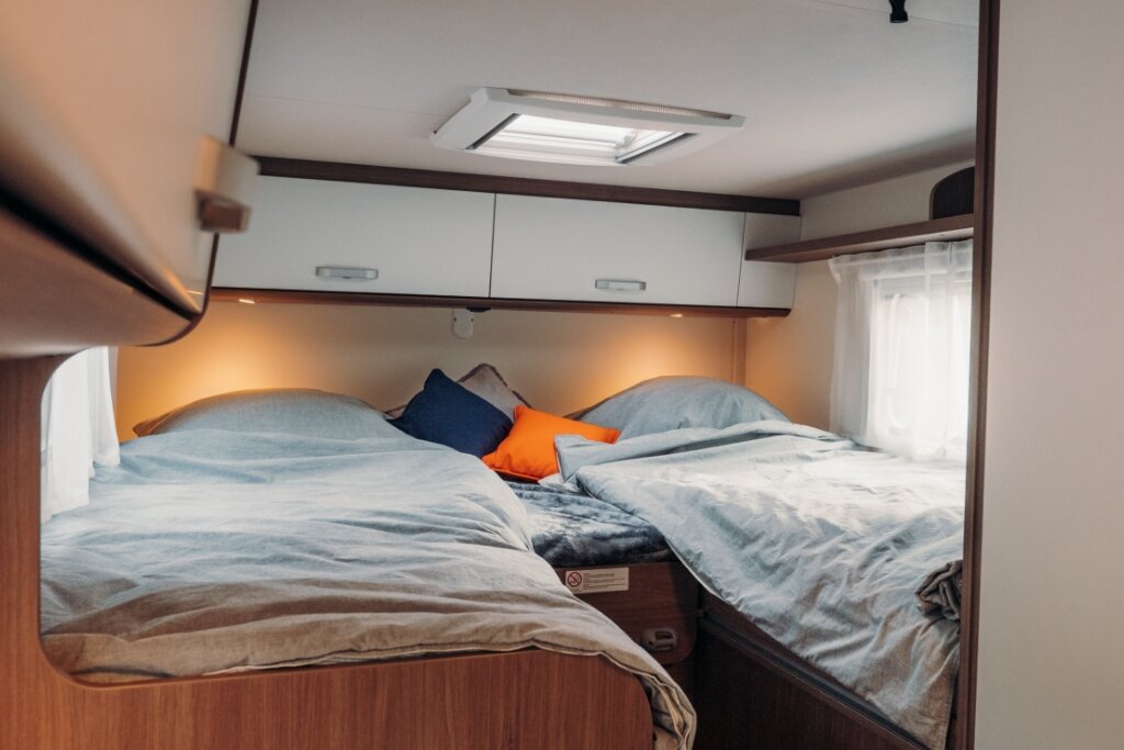 Schlafbereich im Carado Wohnmobil mit zwei Einzelbetten, Dachfenster, Oberschränken und seitlichem Fenster