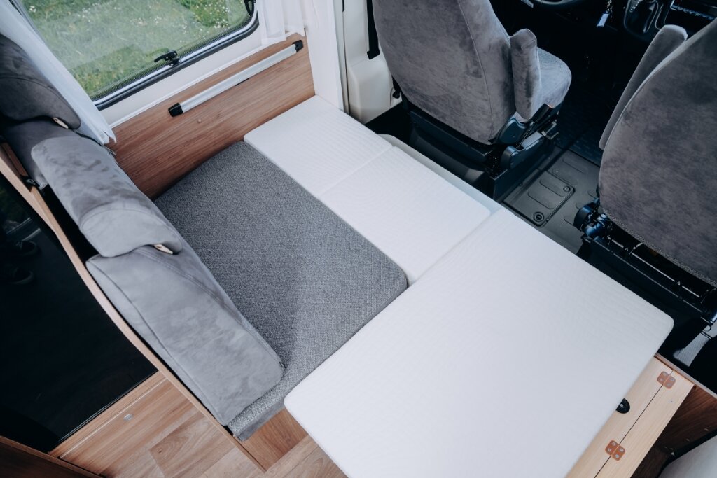 Carado Wohnmobil Innenraum mit umgebauter Sitzbank zur Liegefläche neben drehbaren Fahrerhaussitzen