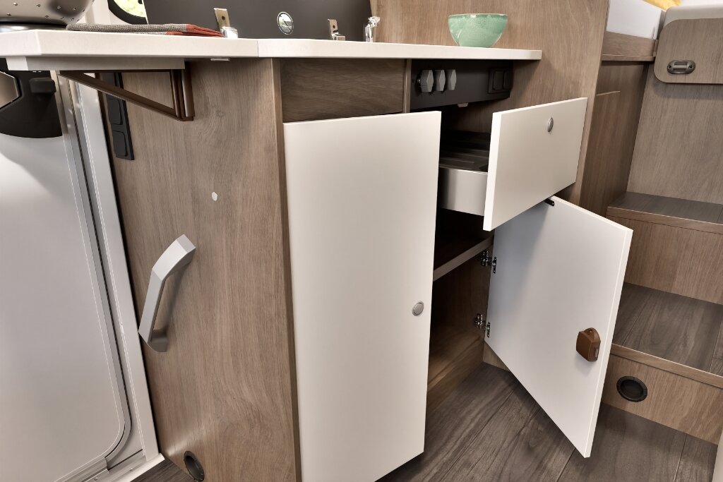 Stauraum im Carado Wohnmobil mit geöffneten Schubladen und Unterschrank neben Küche und Kühlschrank
