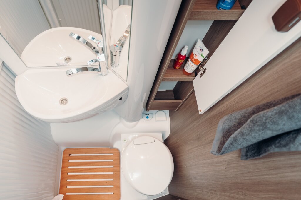 Badezimmer im Carado Wohnmobil mit Waschbecken, Toilette und offenem Badschrank