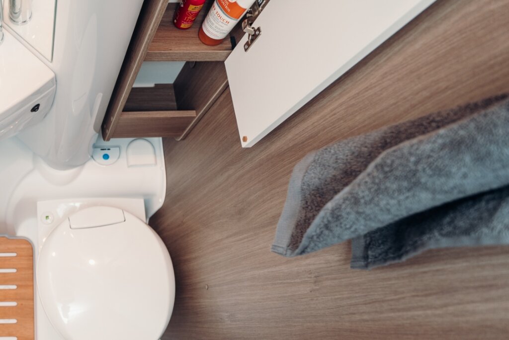 Bad im Carado Wohnmobil mit Toilette, offenem Unterschrank und Handtuch auf Holzdekorboden