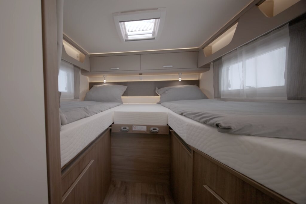 Sleeping area in a Carado motorhome with two single beds, roof window and overhead cabinets