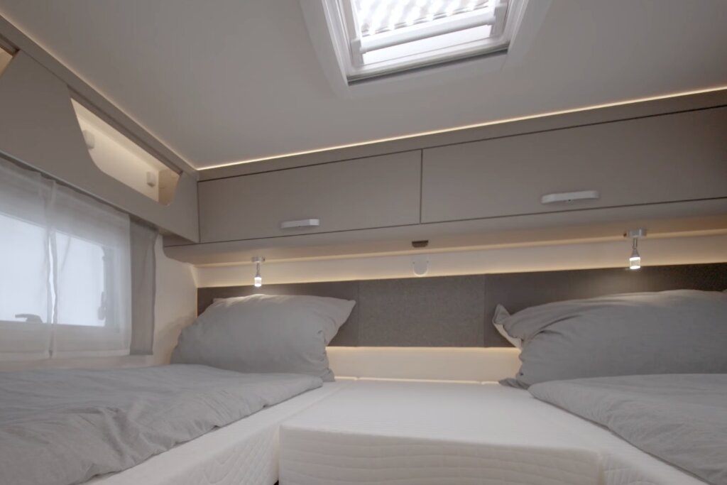 Sleeping area in a Carado motorhome with two single beds, roof window and overhead cabinets