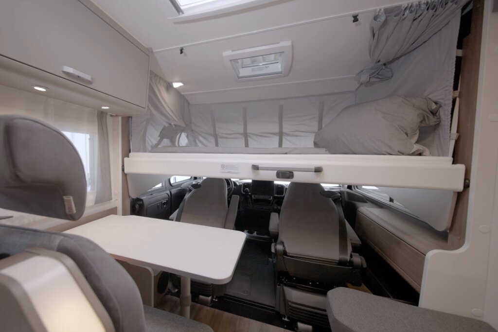 Carado motorhome interior with pull-down bed above the cab and seating area with table