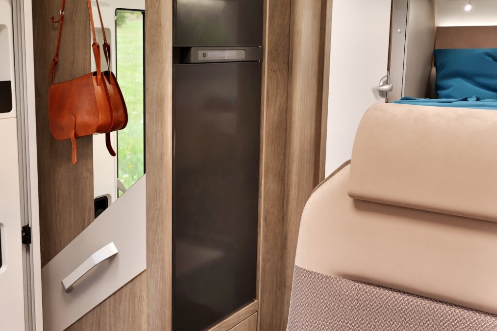 Interior of the Carado motorhome, featuring a tall fridge, wall mirror, hook rail and bed in the background