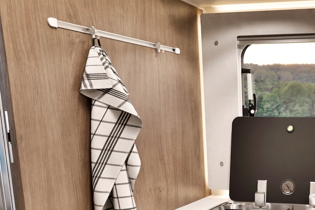 Interior of a Carado motorhome with a towel on a wall-mounted holder beside the window and washbasin